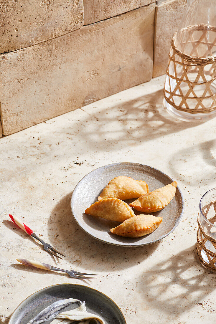 Blick von oben auf leckere spanische Empanadas auf einem Teller, der auf einer Marmorfläche in der Nähe von Schneidegabeln steht, an einem sonnigen Tag