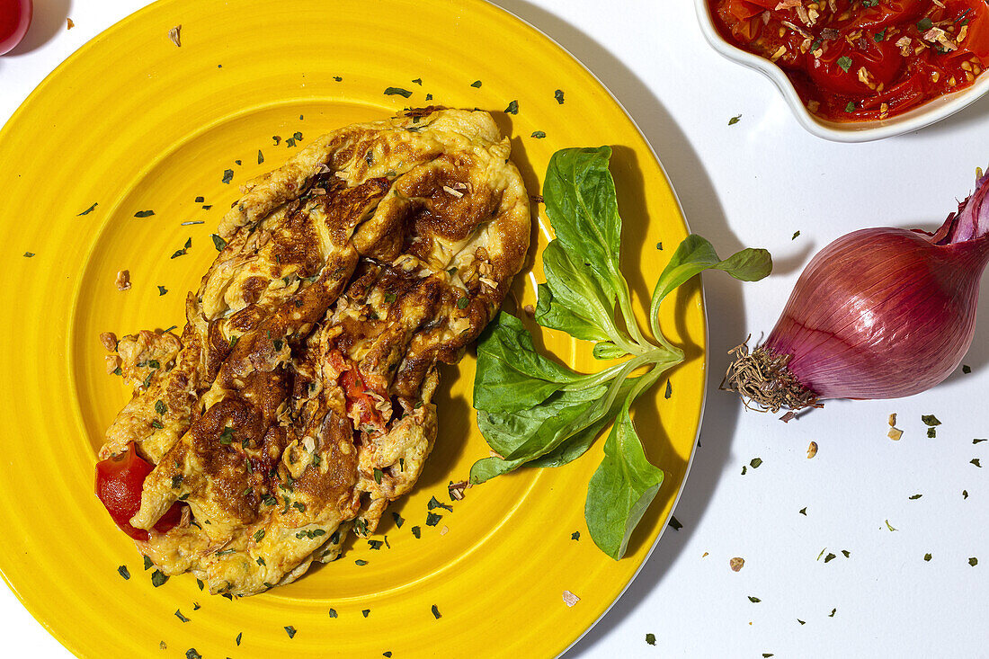 Delicious omelette with chopped parsley on plate against sun dried tomatoes and raw red onion on white background