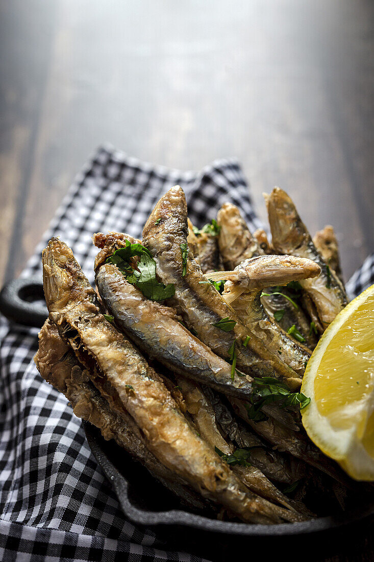 Overhead view of appetizing Fried anchovies with chopped parsley and fresh lemon slice with juicy flesh