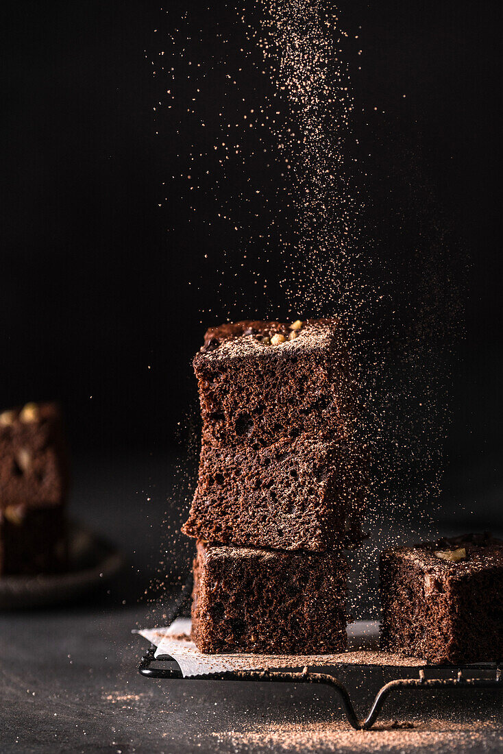 Composition of little stack of tasty sweet brownie cuts with powder on black background