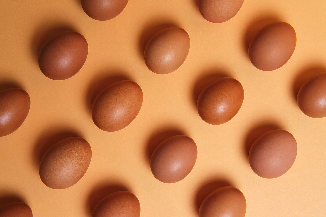 Seamless background of brown eggs placed in rows on orange table in studio