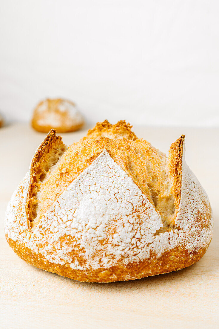 Delicious round shaped bread with flour on golden surface in bakery on white background