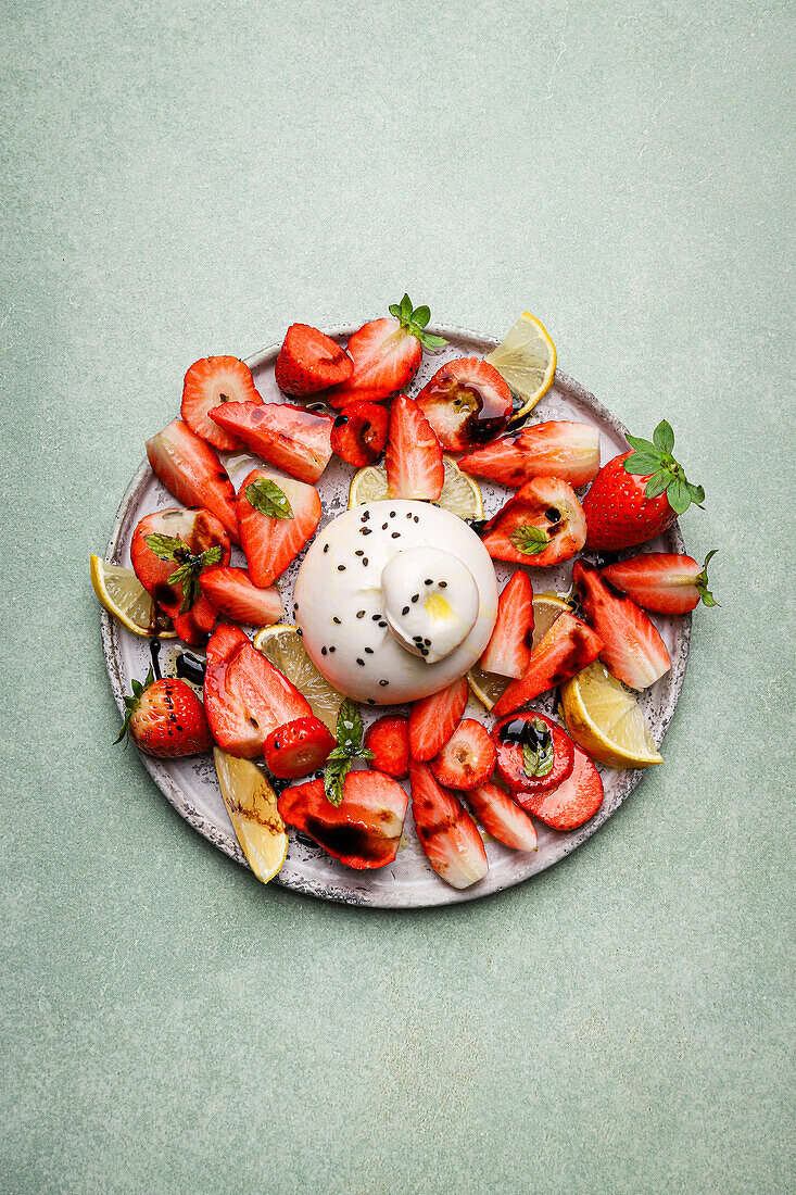 Top view of appetizing fresh strawberries and lemon served with burrata cheese on plate