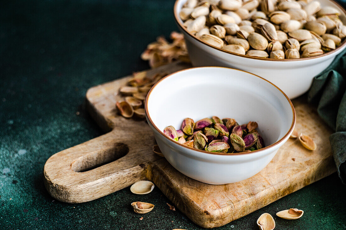 Organic and raw pistachio nuts in the bowls on green table background
