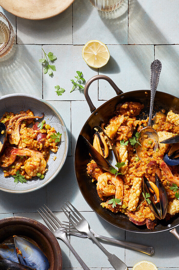 Draufsicht auf eine appetitliche Paella mit Meeresfrüchten, die auf einem Teller serviert und auf eine weiße Fliese gestellt wird