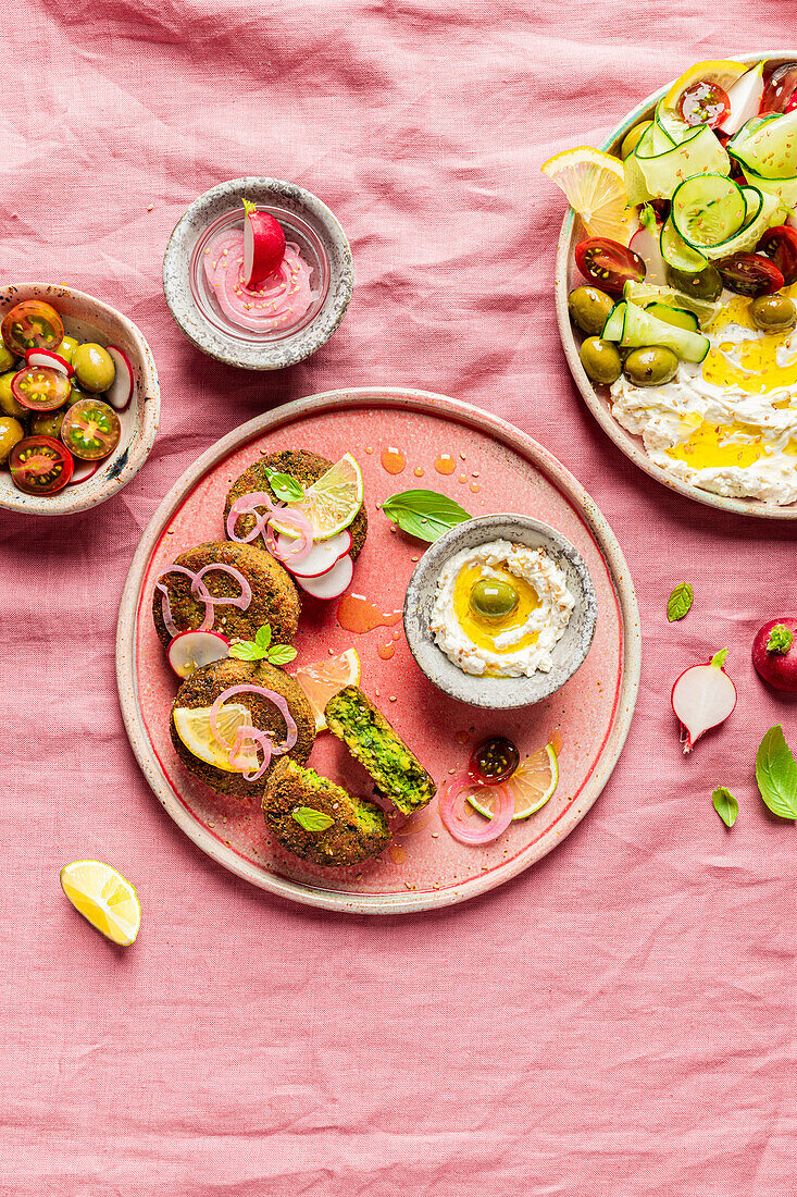 Top view of plate with delicious cream cheese and assorted vegetables placed on napkin near vegan fritters on pink background