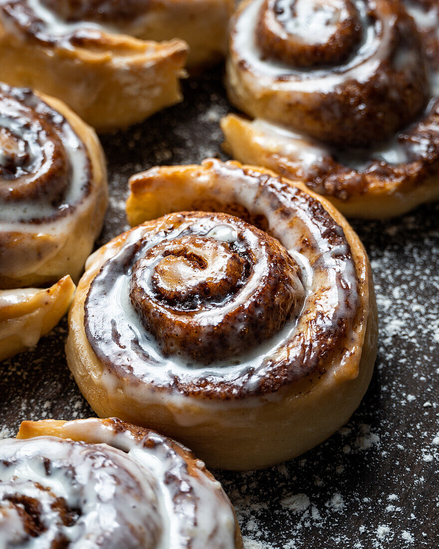 Appetizing baked sweet cinnamon rolls with white cream topping served on table in bakery