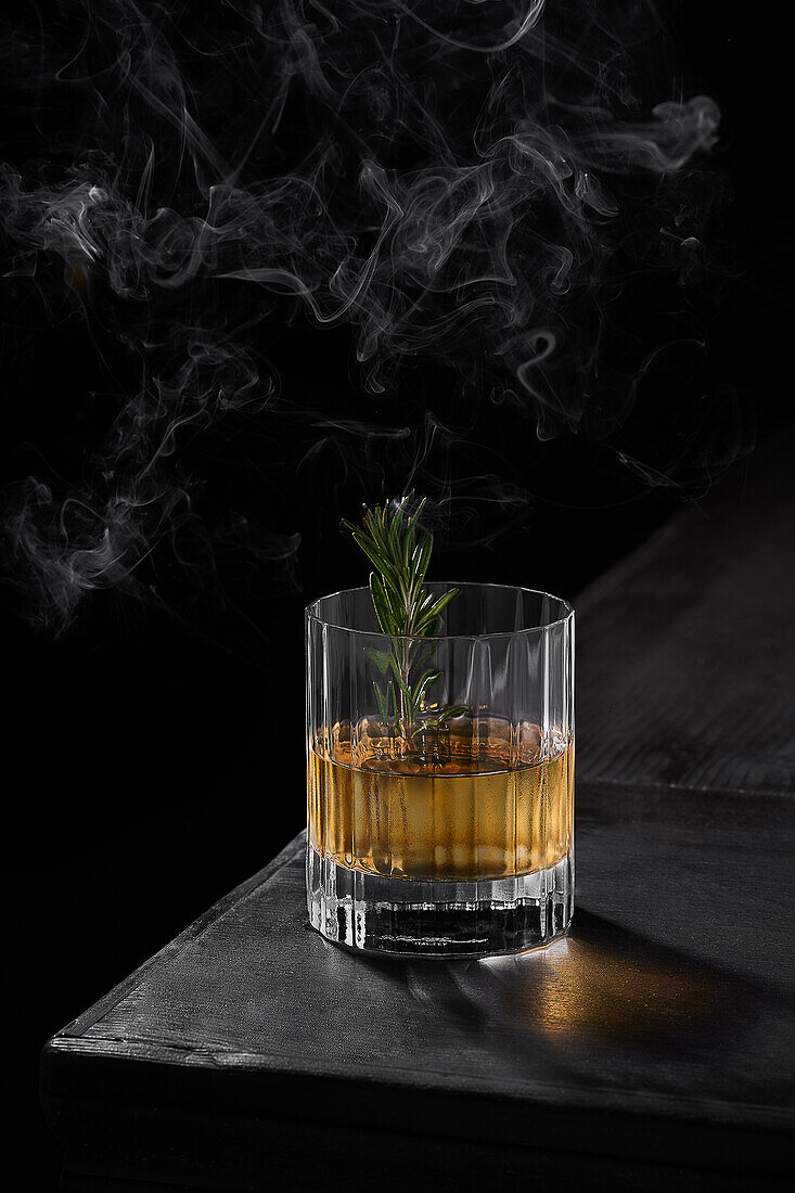 Blick von oben auf ein Glas kalten Whiskey mit grünem Blatt auf einem schwarzen Tisch in einem dunklen, verrauchten Raum