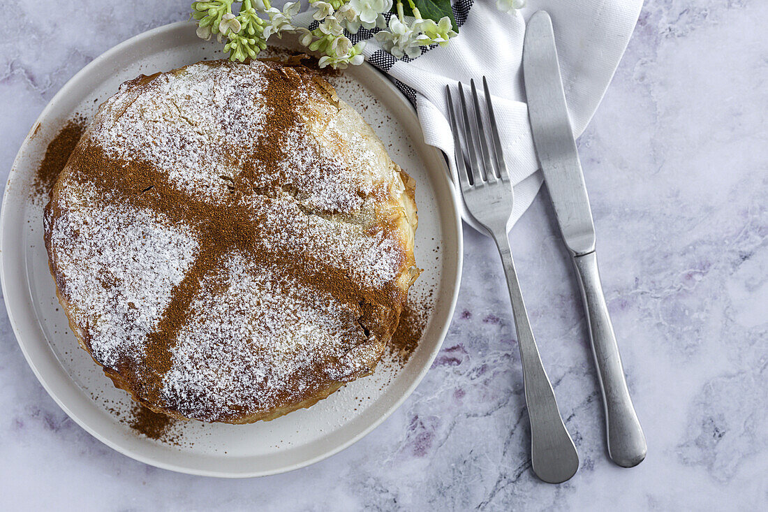 Draufsicht auf eine appetitliche Bastilla mit aromatischen Gewürzen auf einem Tisch in der Nähe eines Blumenzweigs während des Ramadan-Festes