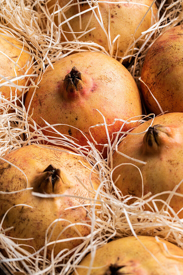 From above of fresh ripe whole orange pomegranates placed together with decorative straw