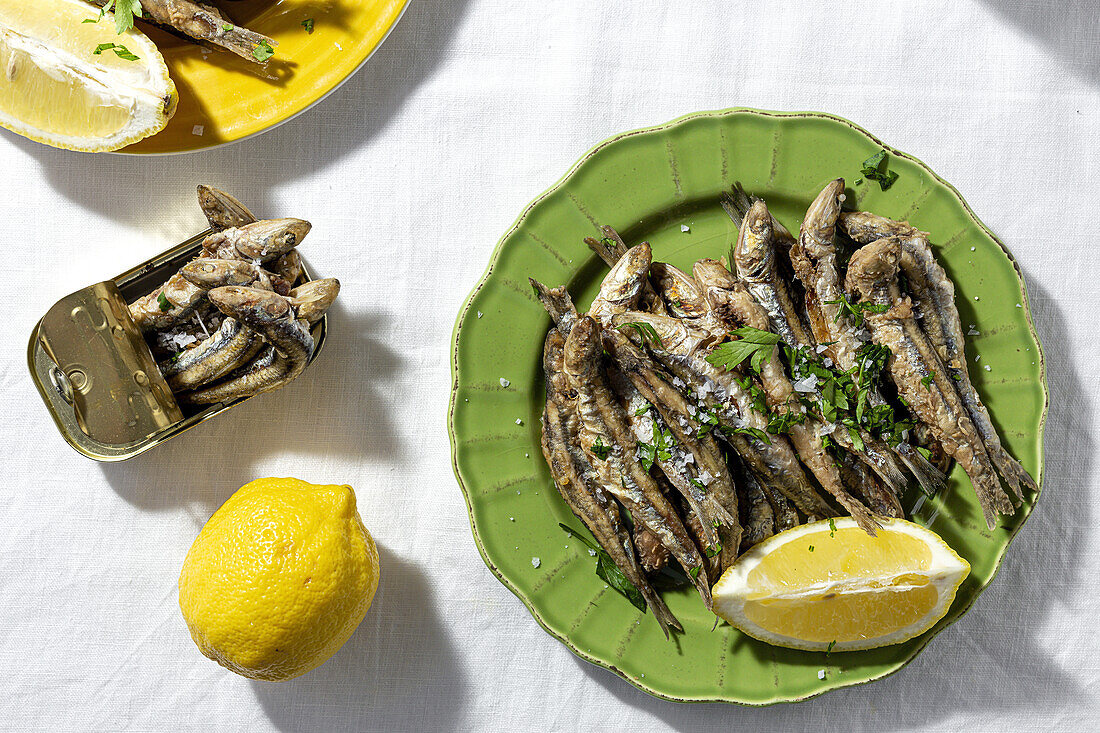 From above of fried and canned anchovies served on table with fresh lemons in restaurant in sunlight