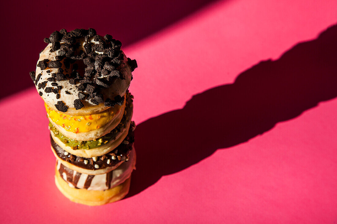 From above tower of donuts of different colors and flavors on pink background