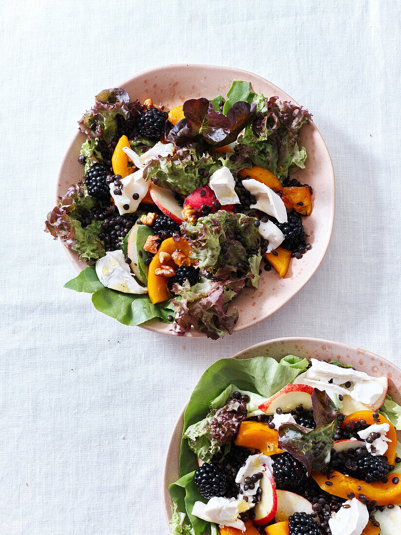 Draufsicht mit zwei Tellern Salat mit gebratenem Kürbis, Beeren und Ziegenkäse. Vegetarisches Festtagsessen