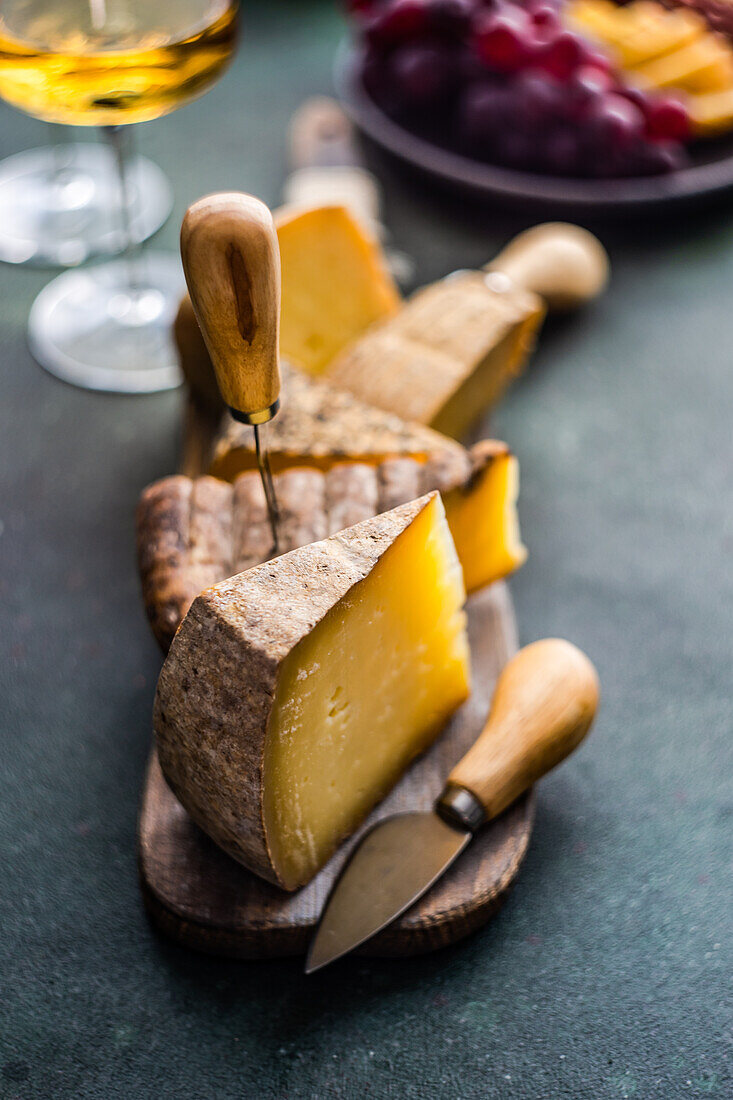 From above cheese variety on the wooden cutting board, fruit plate and wine glasses