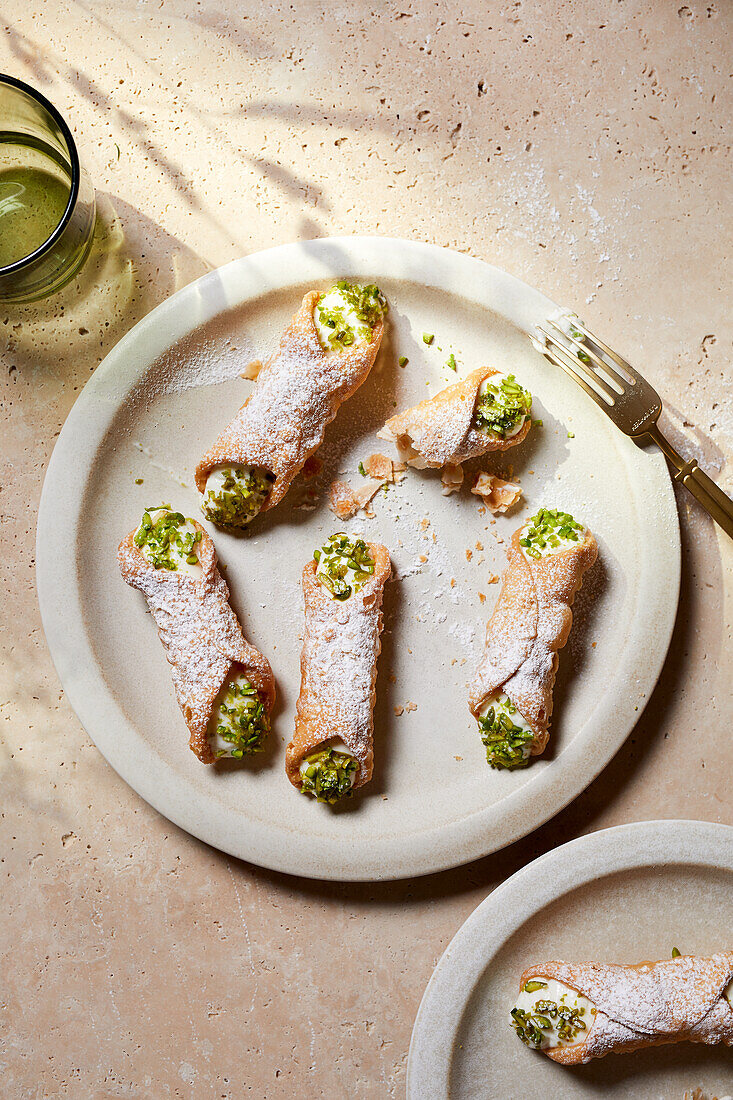Top view of delicious Italian cannoli dessert with cream cheese and pistachio nuts placed on white plate with fork