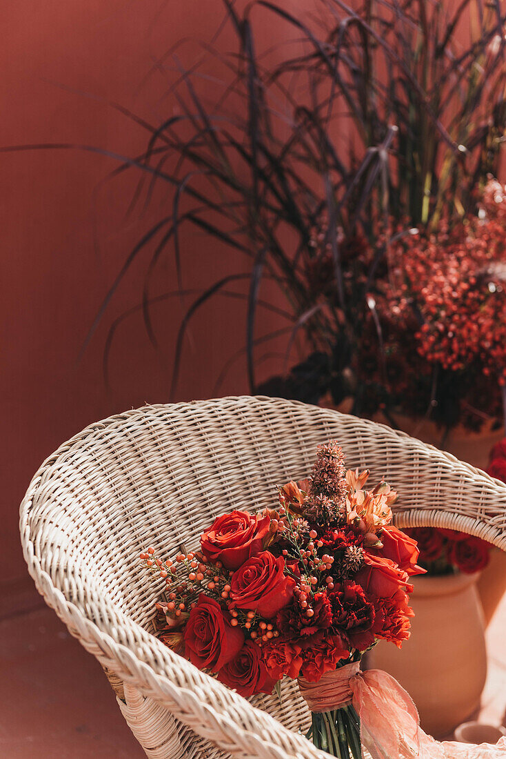 Hoher Winkel von frischen roten Blumen in einem Strauß mit dünnem Band auf einem Korbstuhl bei Sonnenschein