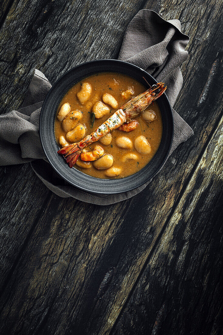 Appetitliche Cremesuppe mit weißen Bohnen und Langusten in einer Schüssel auf einem Holztisch in der Küche (von oben)