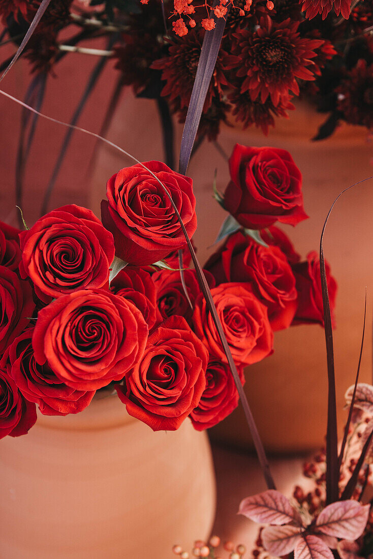 Helle, üppige rote Rosen in einer Tonvase unter Blumen für einen romantischen Anlass oder ein Geschenk