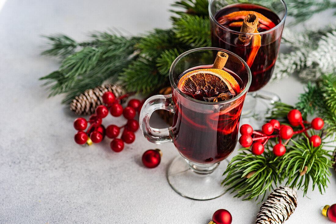 Mulled wine with spices with holiday decoration on white concrete background