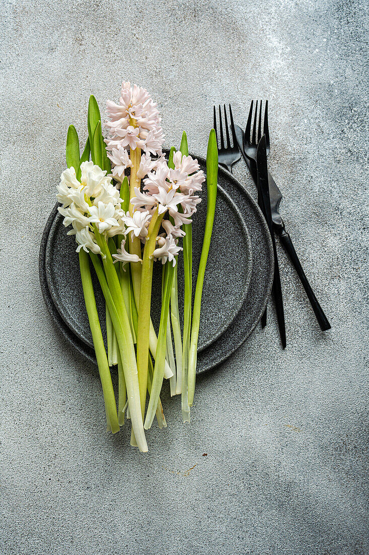 From above spring table setting with hyacinth flower near ceramic plate and cutlery on grey concrete table for festive dinner