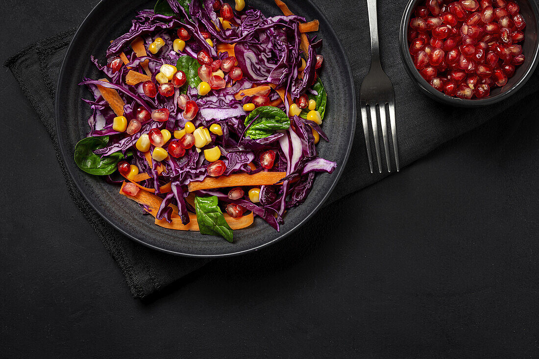 Homemade Purple Cabbage Salad with Corn, Carrots, Pomegranate and Spinach on dark background. Vegan food concept. Healthy food