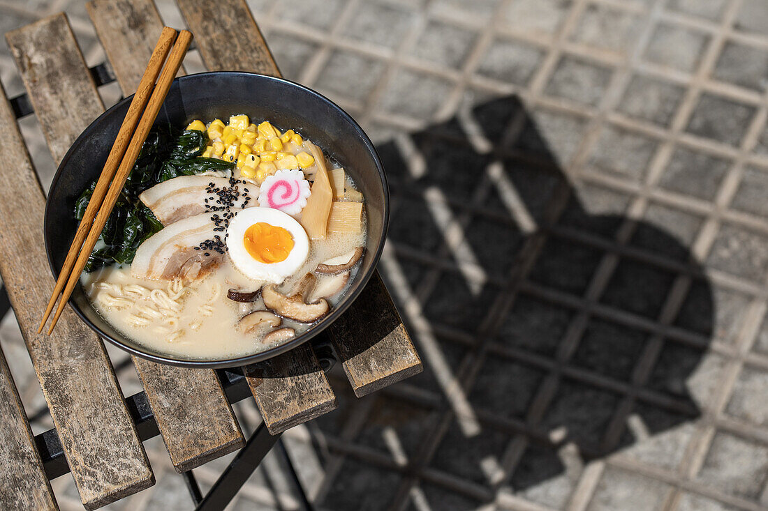 From above of appetizing Japanese ramen with mushrooms and egg served on bowl on corner of table on terrace of restaurant on sunny street in city