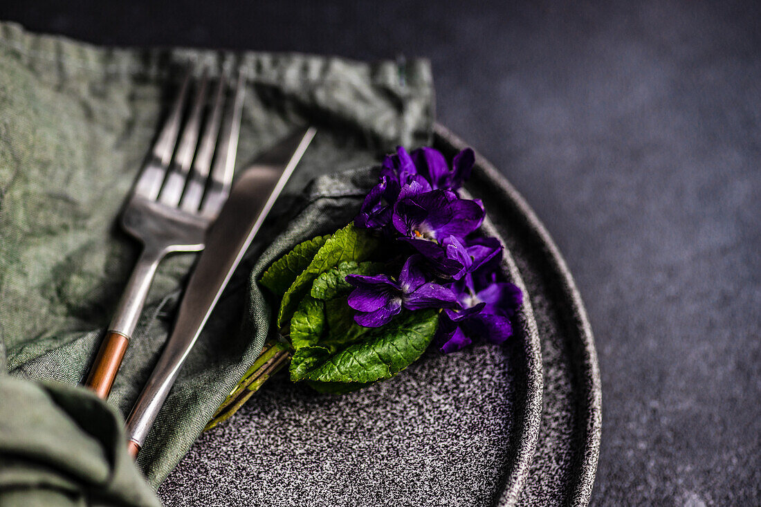 Spring table setting with wild blue viola flower on black plate set