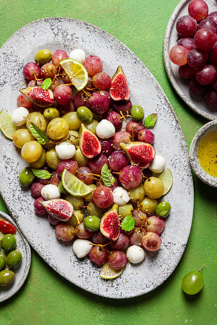 From above fresh ripe grapes, olives, figs and mozzarella seasonal christmas salad placed on plate on green tabletop background