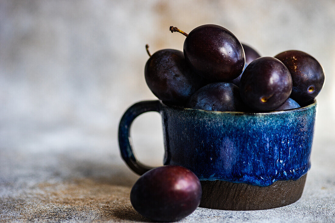 Fresh organic and ripe plum fruits in ceramic cup on concrete background
