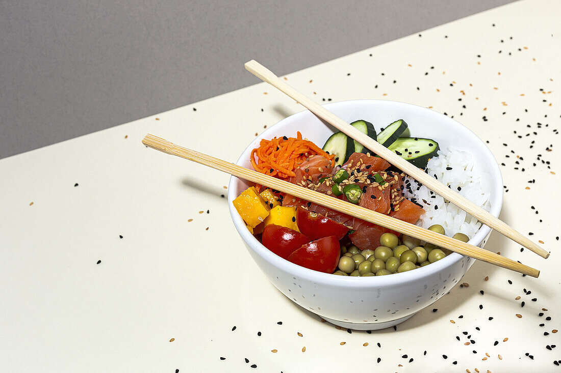 Von oben Bambus-Essstäbchen auf Schüssel mit leckerem Poke-Gericht auf Tisch mit Sesamsamen bedeckt platziert