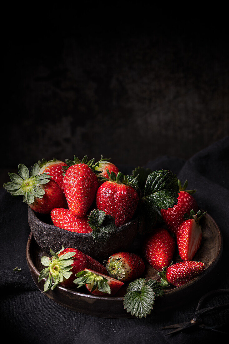 Appetizing fresh ripe juicy strawberries with green leaves served in bowl on dark wooden table with black background
