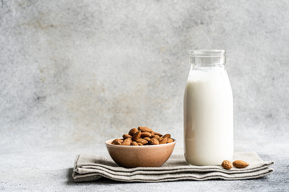 Organic almond milk in glass bottle near ceramic bowl with raw almonds on stone table in the kitchen ready for cooking