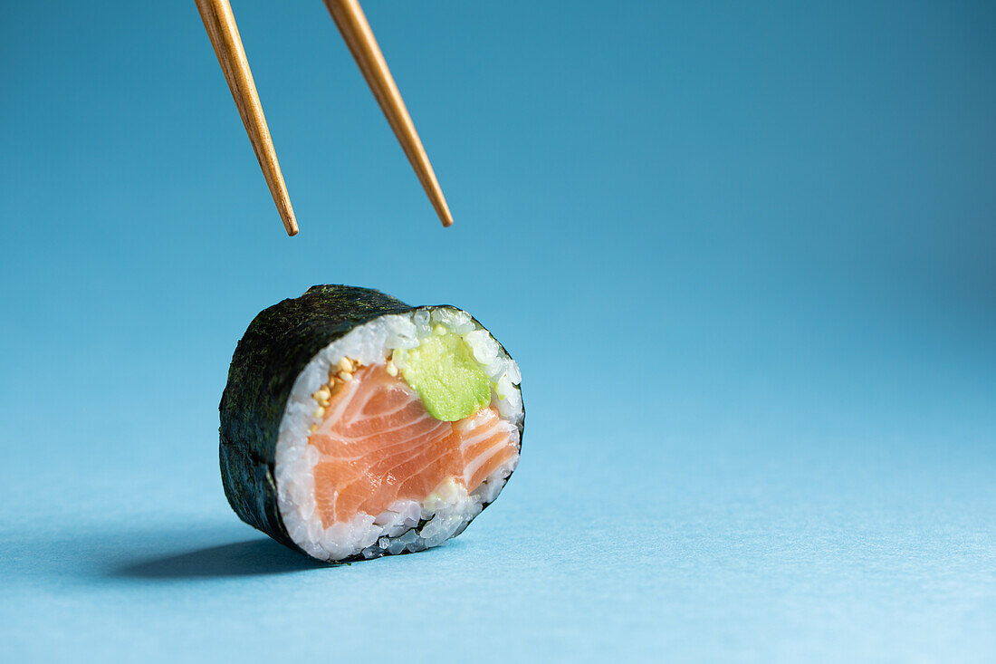 Leckere japanische Futomaki Norwegische Sushirolle mit frischem Lachs und Avocado vor blauem Hintergrund im Studio mit Holzstäbchen