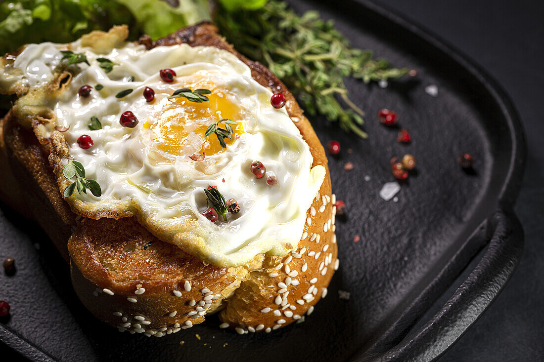 Fried egg on brioche served on tray with fresh lettuce for appetizing breakfast on black background