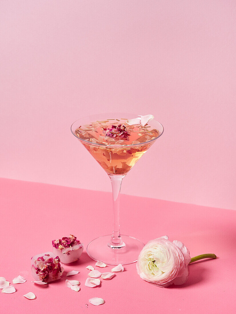 Composition with pink mocktail decorated with rose petals and blooming flower on bright surface