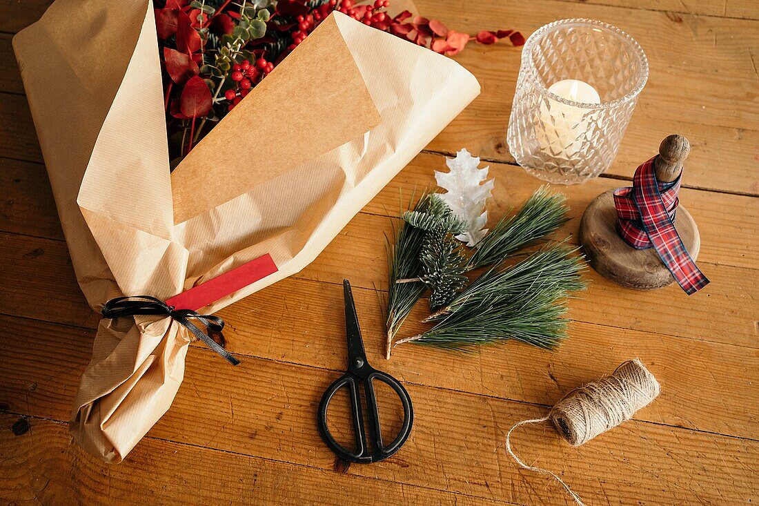 Blick von oben auf einen Weihnachtsstrauß in Geschenkpapier, der in der Nähe von Scheren und Dekorationsmaterial auf einem Holztisch bei Tageslicht platziert ist