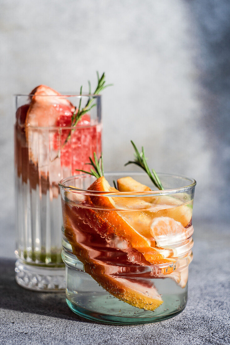 Tropischer Sommercocktail aus Wodka und Sprite mit reifen Früchten und Rosmarin auf grauem Hintergrund