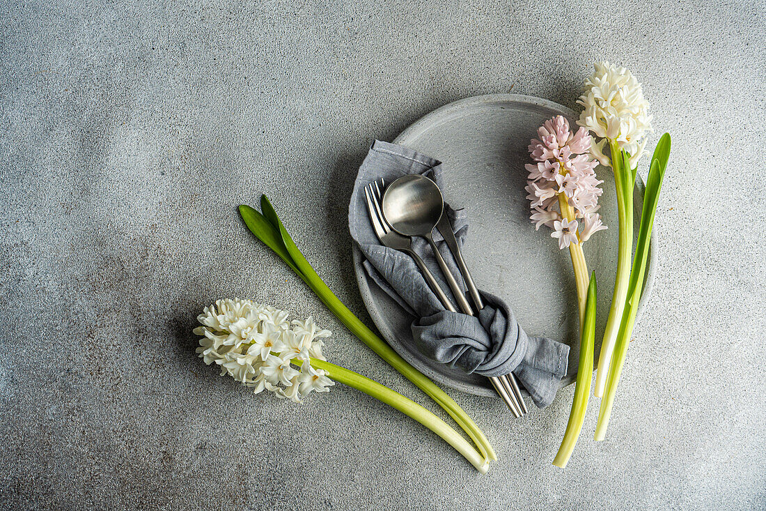 From above spring table setting with hyacinth flower near ceramic plate and cutlery on grey concrete table for festive dinner