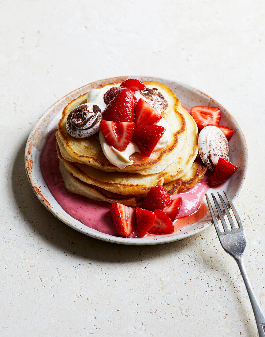Appetizing sweet pancakes with strawberries and cream served on plate near fork with yogurt