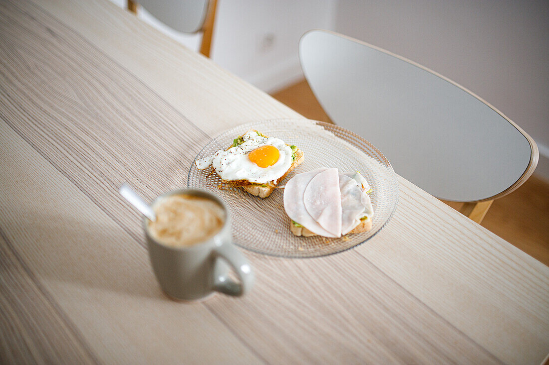 High angle of delicious sandwiches made with fried egg and ham placed on wooden table with cup of hot coffee