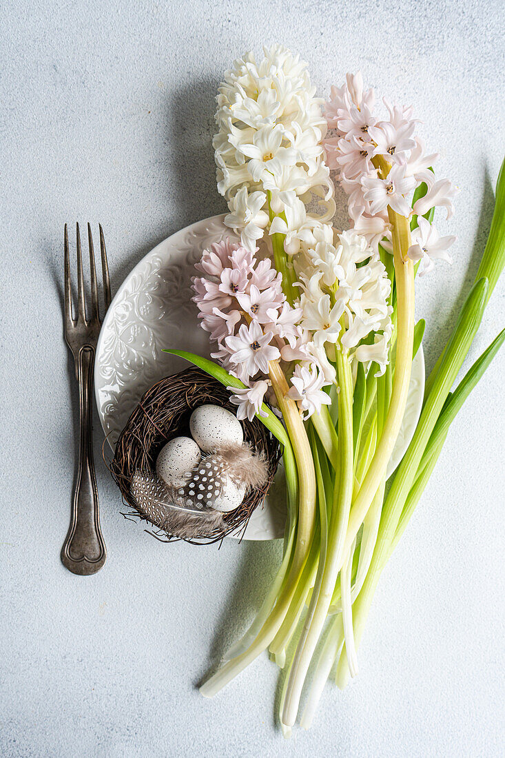 Blick von oben auf ein Osternest mit Eiern auf einem Teller und Hyazinthenblüten auf einem Betonhintergrund