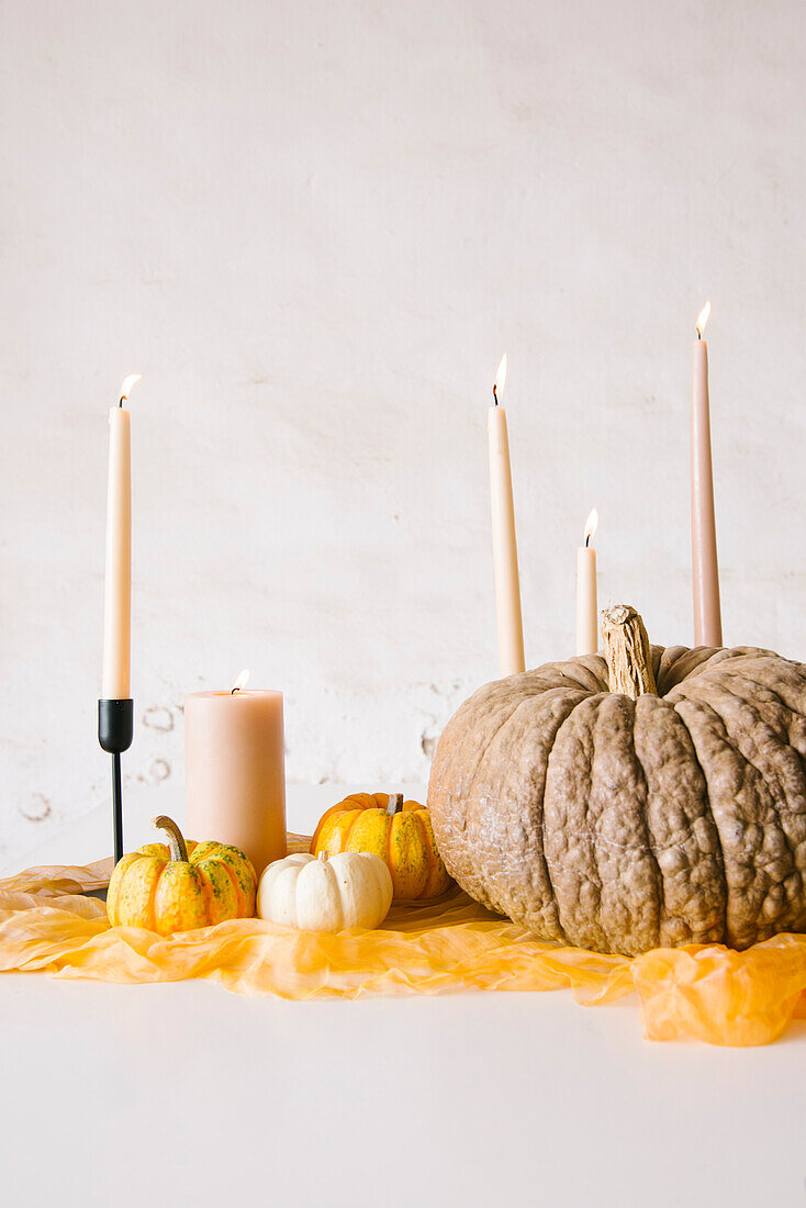 Brennende Kerzen in Stöcken und verschiedene Kürbisse auf einem weißen Tisch während einer Halloweenfeier