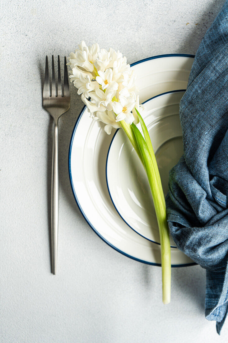 Frühlingshafte Tischdekoration mit Hyazinthenblüten neben Keramiktellern und Besteck auf einem grauen Betontisch für ein festliches Abendessen