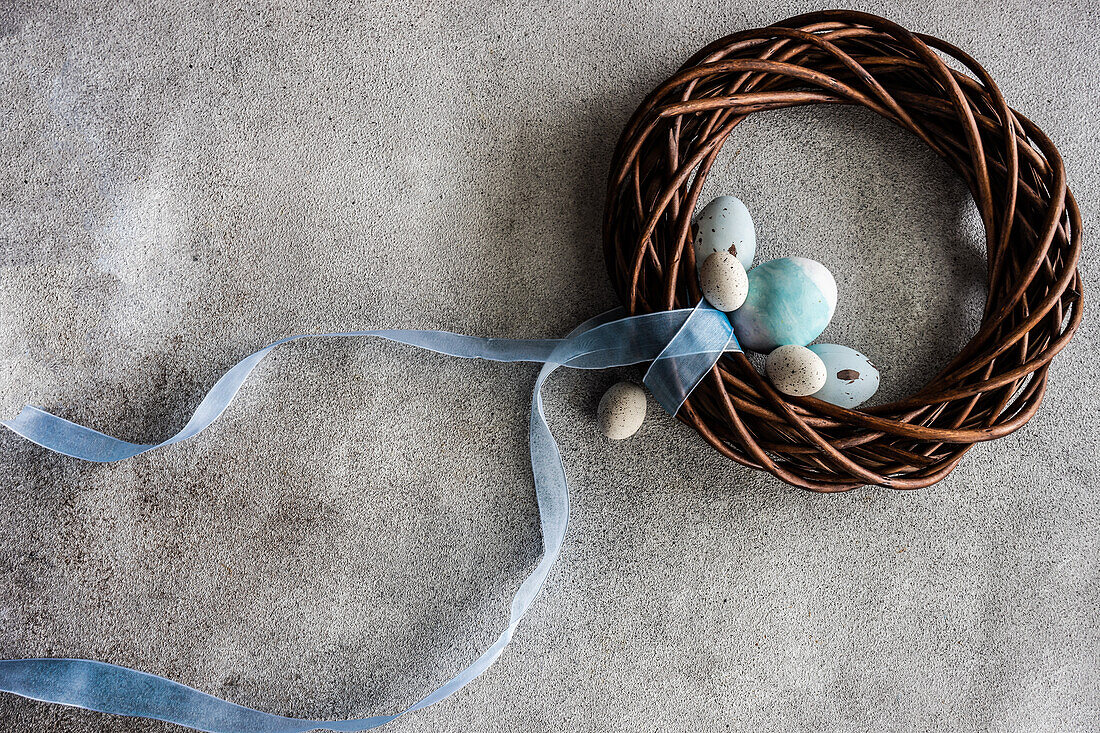 From above easter holiday concept with grape vine wreath decorated with pale blue ribbon on grey concrete background