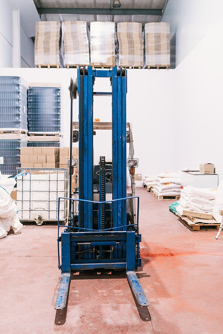 Industrial vehicle on floor against stack of cardboard boxes and plastic containers with bottles of beer in factory