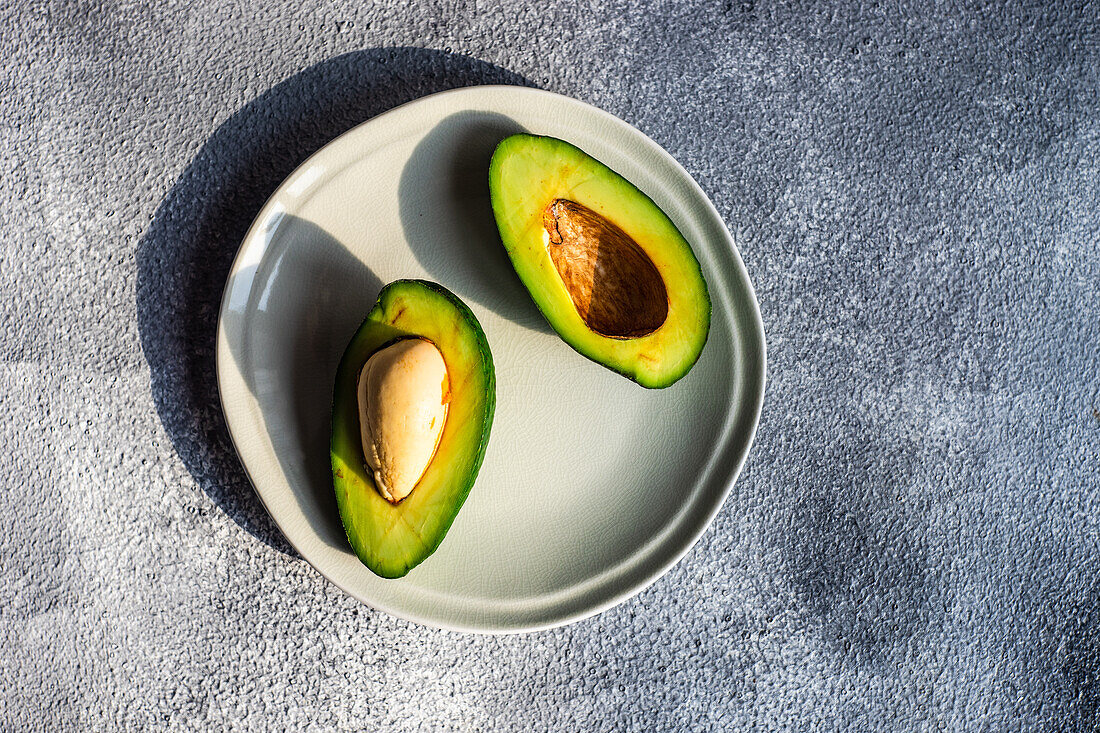 Von oben eine halbe Avocado auf einem Teller auf grauem Betonhintergrund