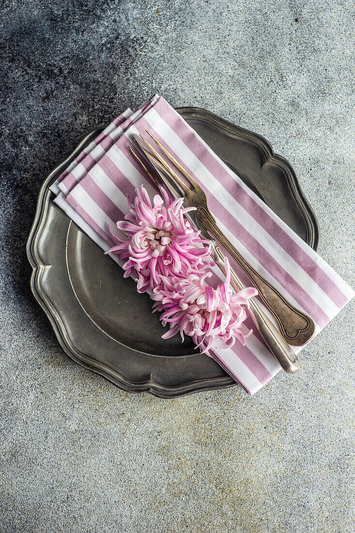 Draufsicht auf einen herbstlich blumengeschmückten Tisch mit Vintage-Tellern und -Besteck, verziert mit lila Chrysanth-Blüten