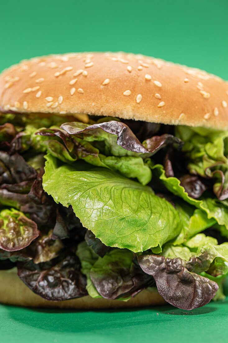 Frisches Burgerbrötchen mit einem Bündel frischer Mesclun-Blätter als Konzept für gesunde Ernährung vor grünem Hintergrund