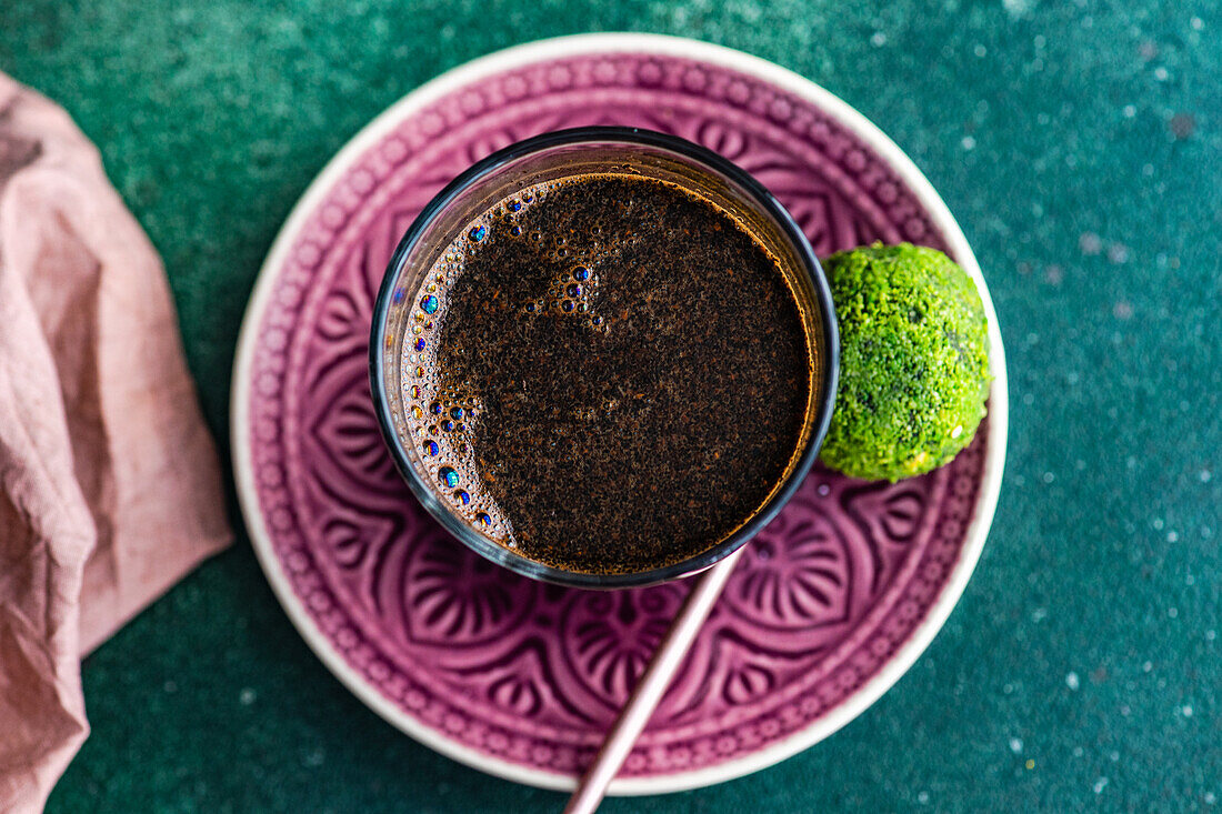 Blick von oben auf ein Glas türkischen Kaffee und traditionelle süße Pakhlava-Kugeln, serviert auf einem grünen Betontisch