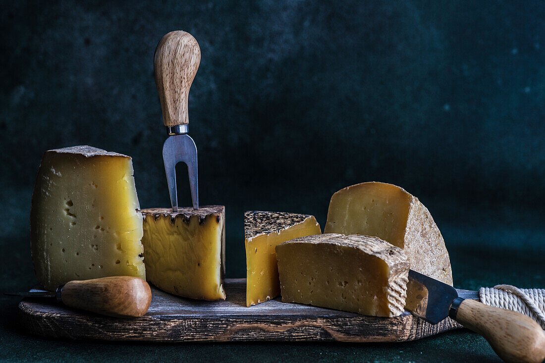 Wooden cutting board with cheese variety on dark concrete background